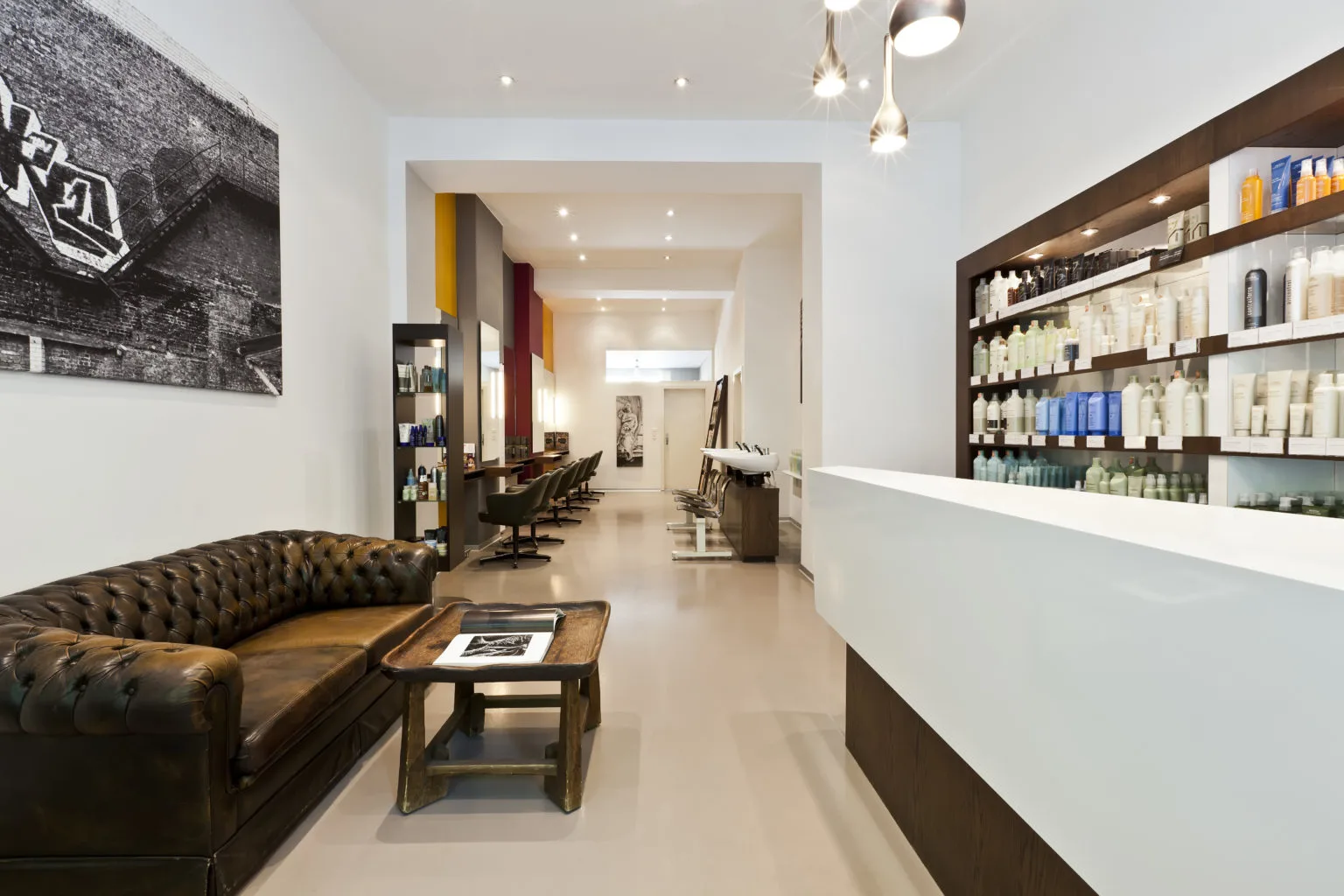 Ruhiger Empfangsbereich des Aveda Exclusive Salon by Eddine Belaid in Zürich Enge mit Chesterfield-Sofa und beleuchtetem Produktregal
