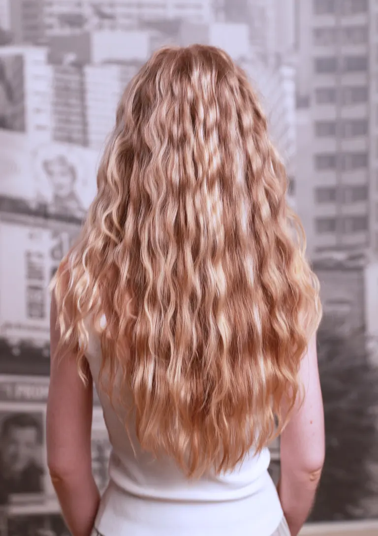 Long strawberry blonde waves with movement, seen from behind against the city wallpaper in Eddine Belaid's salon